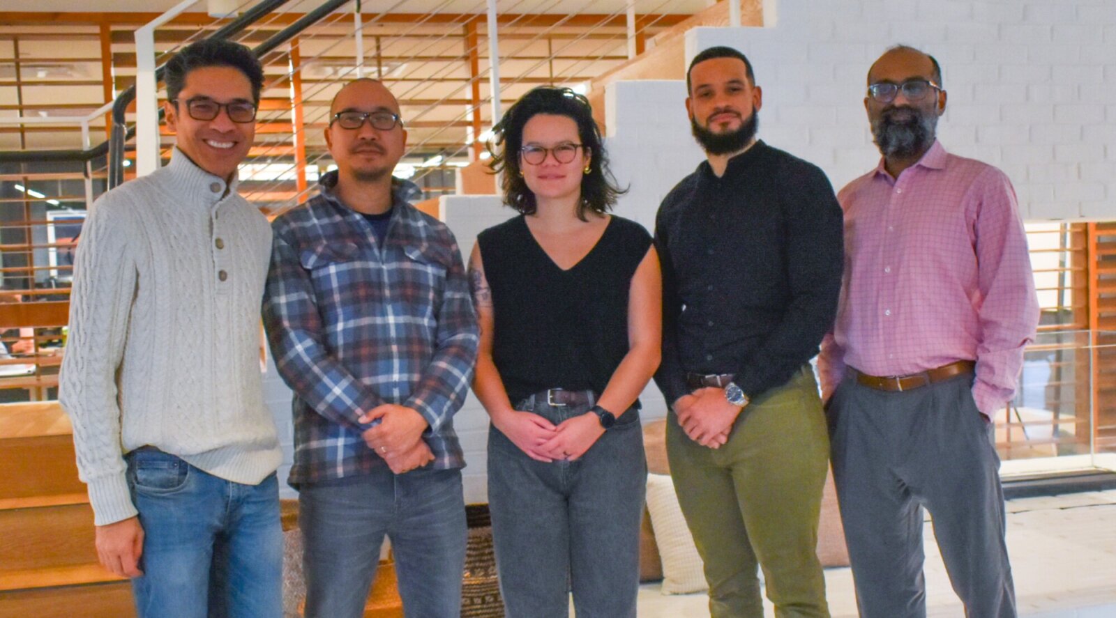 From left to right is CEO George Guerrero, Co-founder Alex Saingchin, COO Mika Weinstein, with members of the Gilmore Khandar Law Firm Trey McKinney and Parag Khandar. They are standing in an office near a set of stairs smiling at the camera.